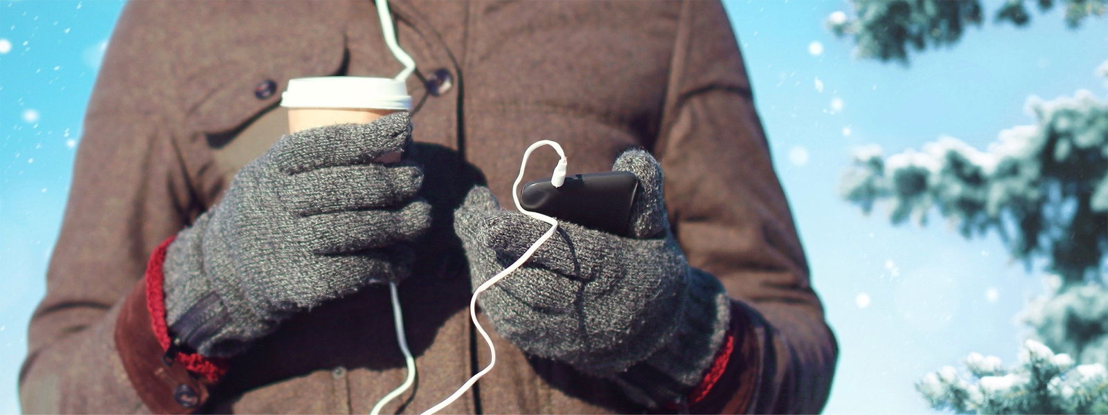 Ein Mann ist draußen im Winter und hält einen Kaffeebecher und sein Handy 