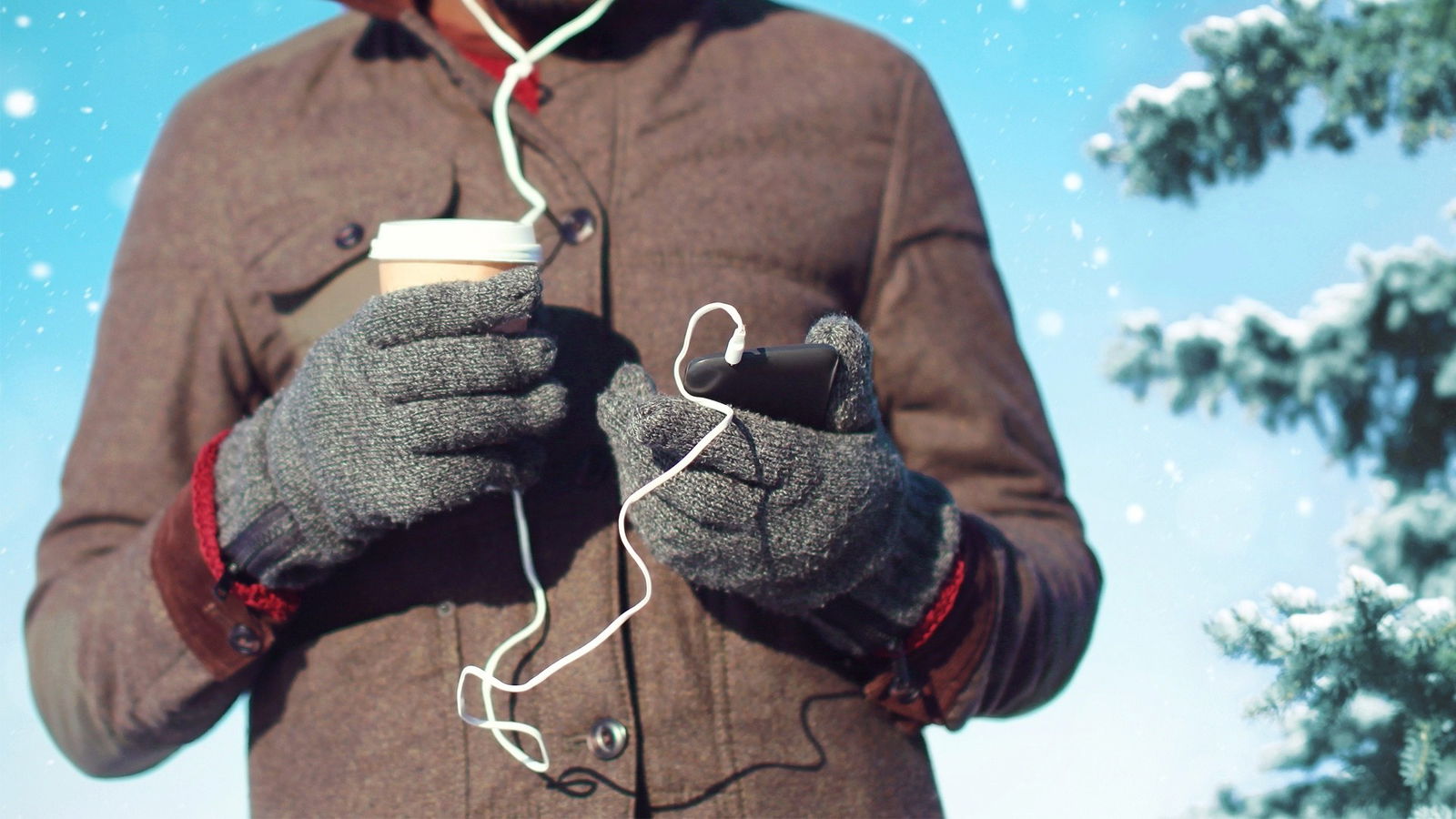 Ein Mann ist draußen im Winter und hält einen Kaffeebecher und sein Handy 